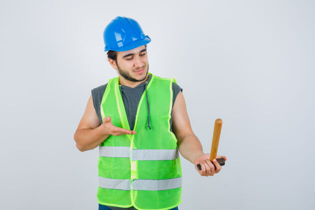 男性年轻的建筑工人穿着工作服拿着锤子 看上去很高兴正视图好看有趣制服