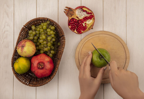 板俯视图：女人在砧板上切青苹果 在白墙上的篮子里放石榴 苹果和葡萄葡萄顶部女人