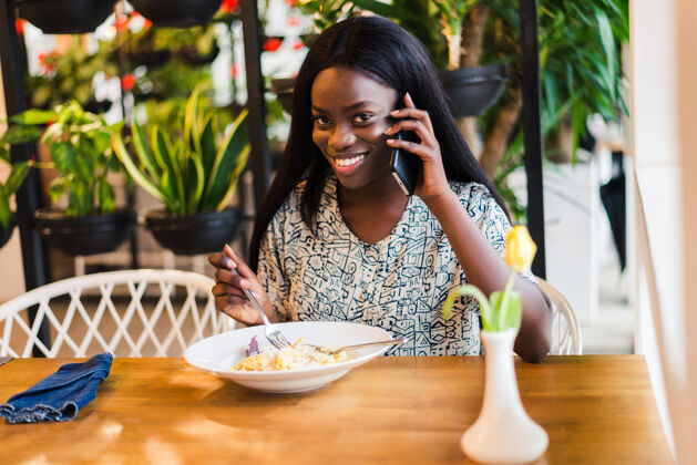 电话非洲年轻女子吃意大利面和打电话的画像人营养情感