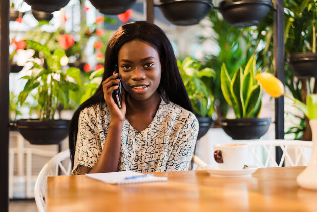 人微笑的非洲年轻女子坐在咖啡馆打电话的画像手机候选人坐着