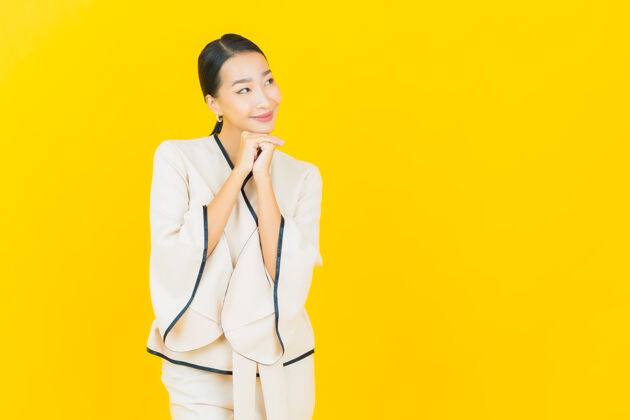 商业美丽的亚洲年轻商业女性在黄色墙上穿着白色西装微笑的画像正式人脸