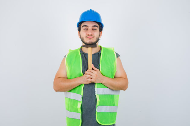 男性年轻的建筑工人穿着工作服 下巴下拿着锤子 看上去很自信 正对着前方成人严肃时尚