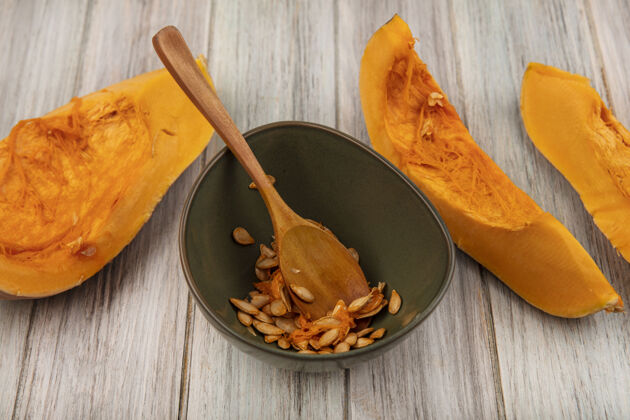 营养顶视图美味的橙色南瓜片与种子在一个灰色的木制表面木勺碗食物碗切片