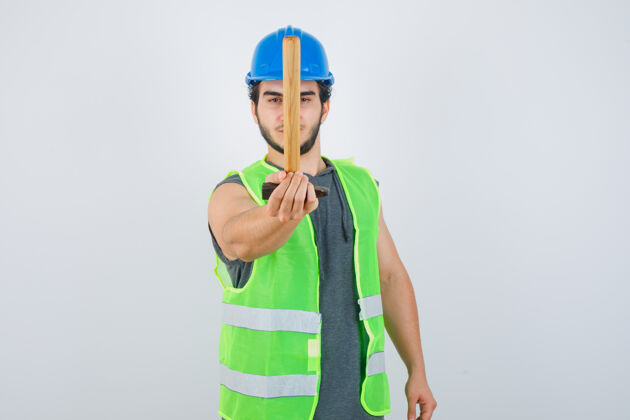 刮擦年轻的建筑工人穿着工作服 对着镜头抓着锤子 看上去很自信 正对着镜头制服模特帅气
