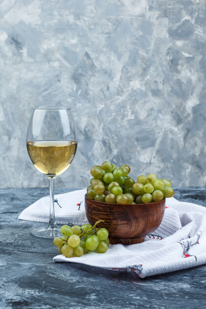 毛巾侧视图绿色葡萄在碗里与一杯葡萄酒在肮脏的石膏和厨房毛巾的背景垂直石膏美味健康