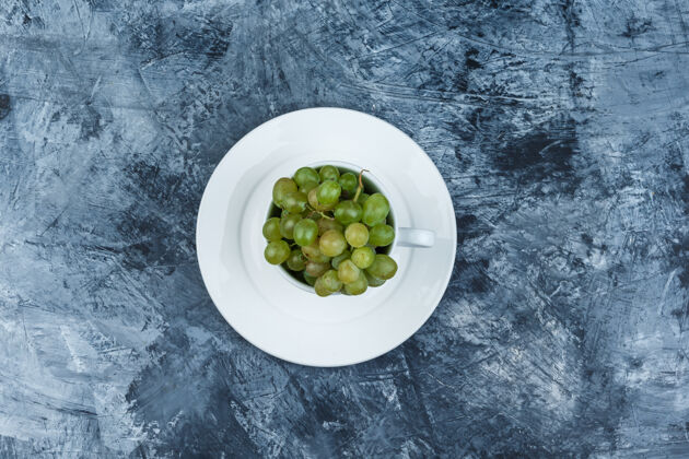 葡萄藤绿色葡萄在一个白色的杯子与板顶视图在一个肮脏的石膏背景盘子秋天咕噜