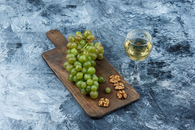 饮食平放白葡萄 核桃在砧板上 酒杯放在深蓝色大理石背景上水平分支营养葡萄藤