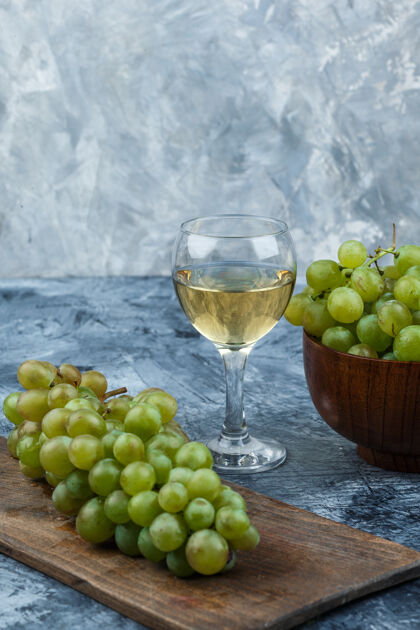 新鲜一组葡萄酒 砧板上的葡萄和碗里的白葡萄 背景是深蓝色和浅蓝色的大理石特写镜头浆果葡萄板