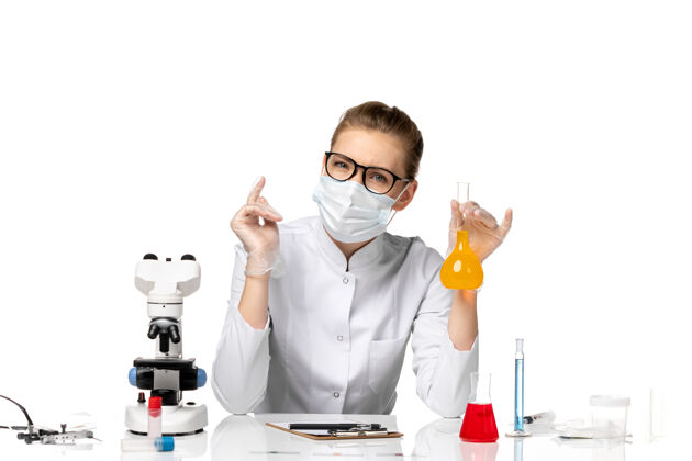 疾病前视图穿着医疗服的女医生戴着面罩 因为科维德在白色办公桌上用溶液工作穿着前台套装