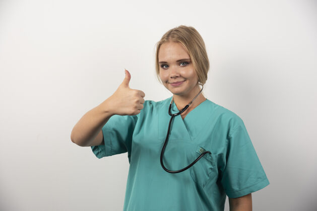 职业微笑的女医生在白墙上竖起大拇指专业女孩女
