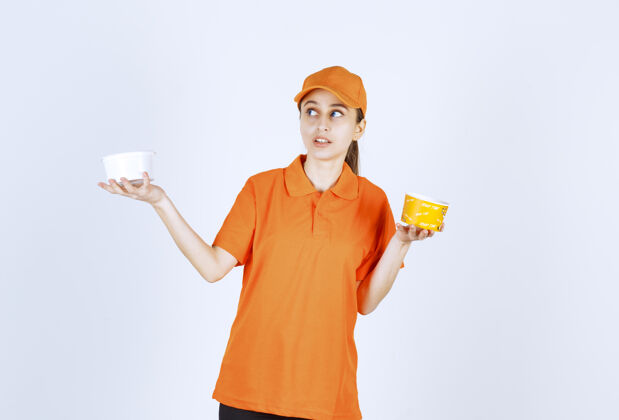 雇员身着橙色制服的女快递员双手捧着塑料杯和黄色面杯船运聪明人姿势