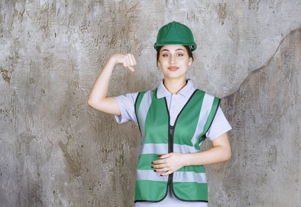 模特穿着绿色制服和头盔的女工程师展示她的手臂肌肉工作场所强壮员工