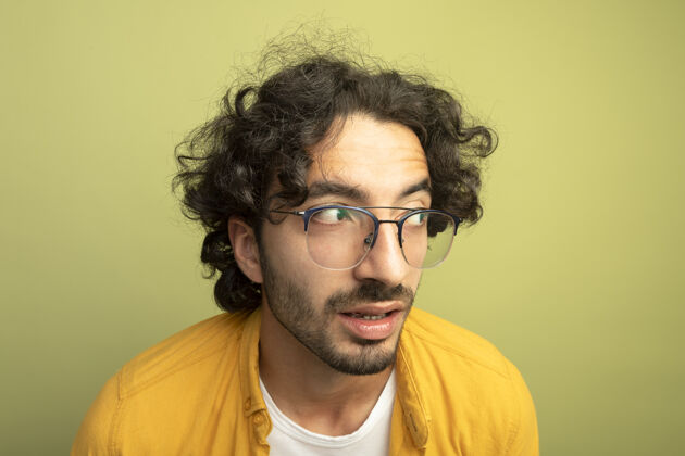 印象特写镜头印象深刻的年轻英俊的白人男子戴着眼镜看着一边孤立的橄榄绿墙上穿着年轻眼镜