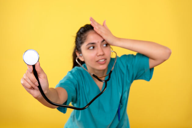 成人黄墙上年轻女医生戴着听诊器将韩寒的头戴在头上的正面图肖像快乐听诊器