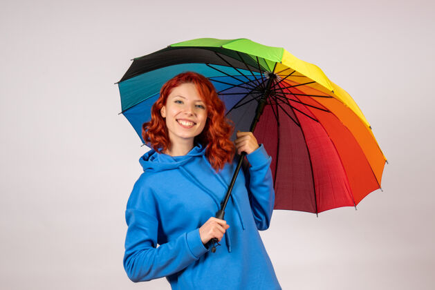 掩护白色墙壁上带着彩色雨伞的年轻女性的正视图年轻女性庇护所雨