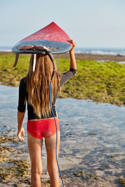 冲浪者后视图中的苗条女子身穿红色比基尼 留着长发 头顶冲浪板皮带人冲浪女孩