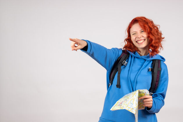 微笑年轻女性的正面图 白色墙上有背包和地图人游客假期