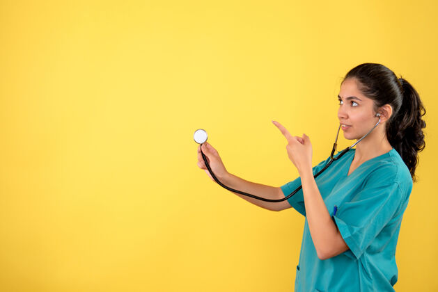 人年轻女医生的正视图 听诊器指着黄色墙上的东西成人前面人