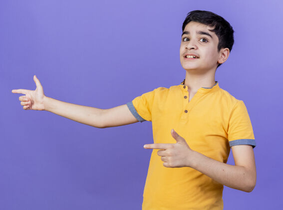 男孩令人印象深刻的年轻白人男孩指着隔离在紫色墙上的一侧男人印象手势
