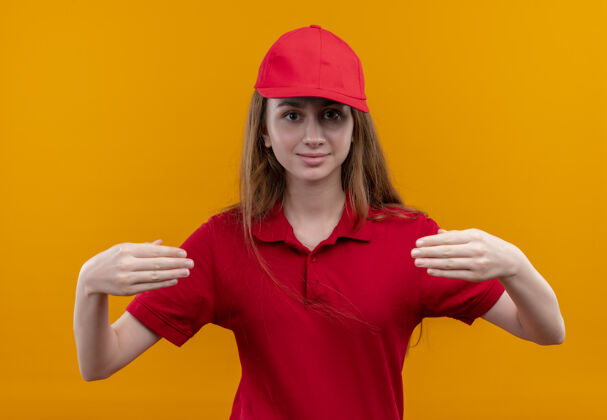 抱着穿着红色制服的年轻送货女孩假装在孤立的橙色墙上拿着什么东西女孩制服年轻