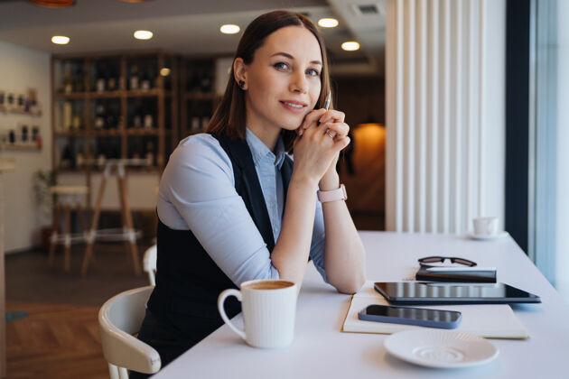 新闻体贴的女人拿着咖啡杯坐在自助餐厅里中年女人一边喝茶一边思考一边喝咖啡一边放松和思考女性杯子女士