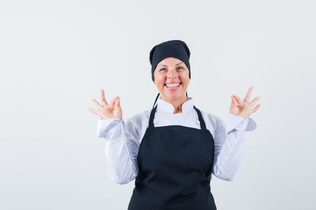 可爱身穿黑色厨师制服的金发女人 双手显示ok标志 看起来很开心 正面视图化妆护理漂亮