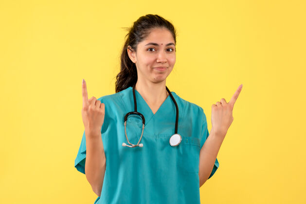 指尖年轻女医生用手指指着黄色墙壁的正视图健康护士年轻女医生