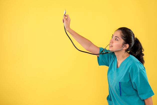 听诊器黄色墙上带听诊器的年轻女医生的正面图年轻女医生前面人