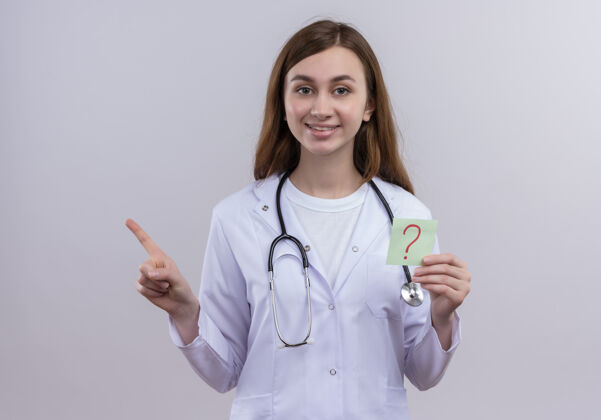 指着面带微笑的年轻女医生 穿着医用长袍 手持听诊器 手里拿着写着问号的纸条 指着隔离的白墙上的左边长袍医生女人