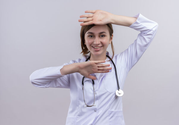 穿面带微笑的年轻女医生穿着医用长袍和听诊器把双手放在隔离的白色墙壁上和头下长袍医生头