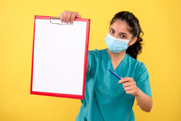 面具黄色隔离墙上拿着剪贴板的年轻女性的正视图护士药医院