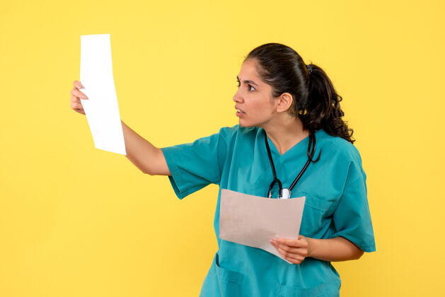 人身着制服的年轻女医生正对着黄色墙壁检查文件成人快乐前面