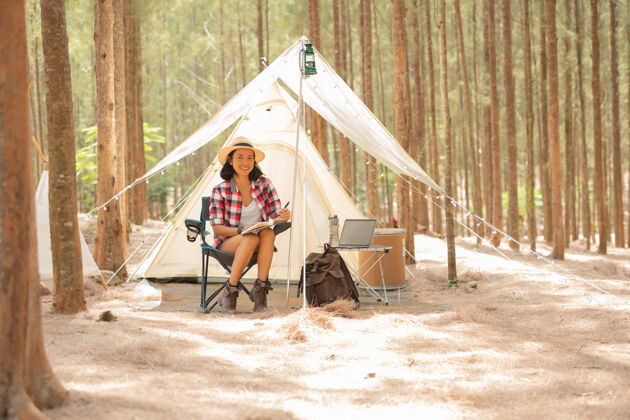 帽子年轻的女游客坐在帐篷旁边看书人和生活方式的概念旅游和冒险主题女游客肖像公园景观山