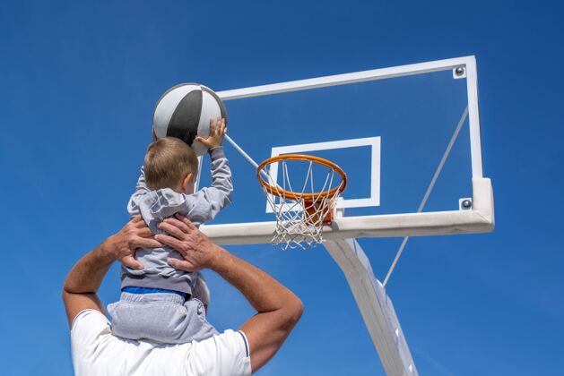 微笑一个孙子坐在爷爷的肩膀上 把篮球扔进篮球圈孩子老人运动