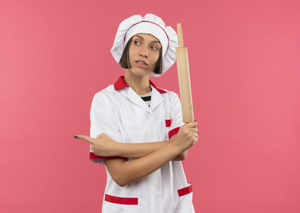 别针自信的年轻女厨师 身着厨师制服 手持擀面杖 看着并指着粉色的一侧 并留有复印空间信心复制空间