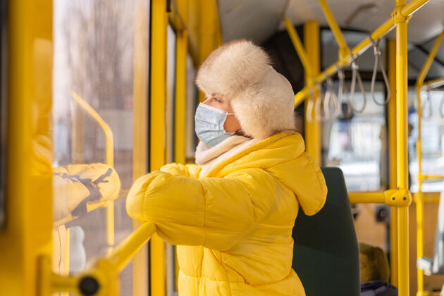 女性一个穿着暖和衣服的年轻女子在一个冬天的城市公共汽车上的明亮的阳光肖像安全检疫车站