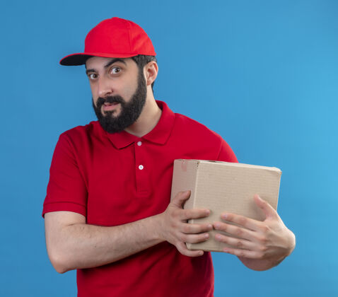 盒子自信的年轻英俊的白人送货员穿着红色制服 戴着帽子 拿着一个蓝色的纸箱男人帅气穿