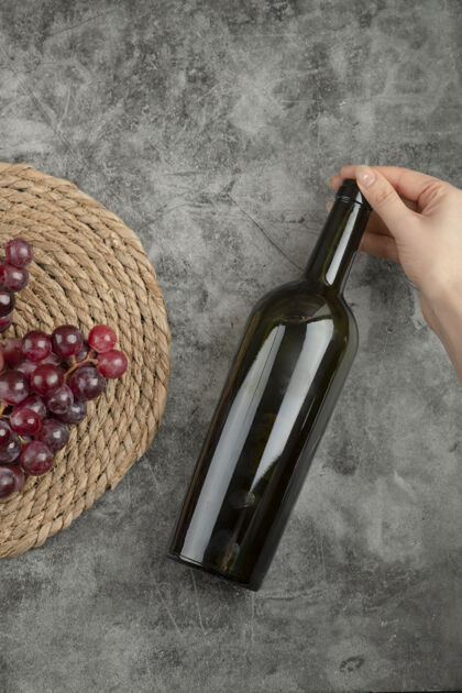 新鲜一簇红葡萄和一位女士手拿酒瓶放在大理石表面上瓶子农业明亮