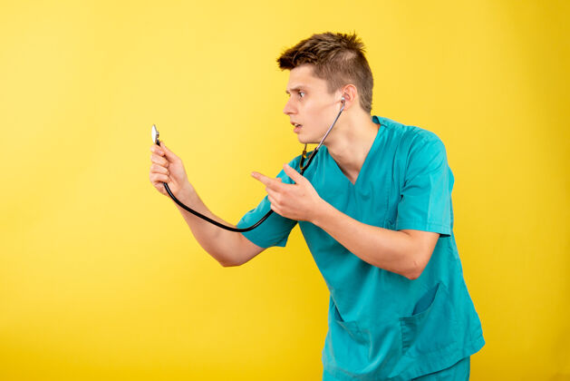 成人前视图年轻男性医生穿着医疗服 黄色背景上有听诊器微笑人药