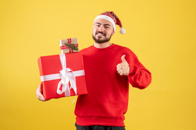 成人黄色背景上手持圣诞礼物的年轻男性正面图人帽子雪