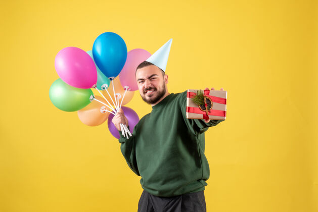 礼物正面图年轻男子手持五颜六色的气球 呈现黄色气球年轻男性年