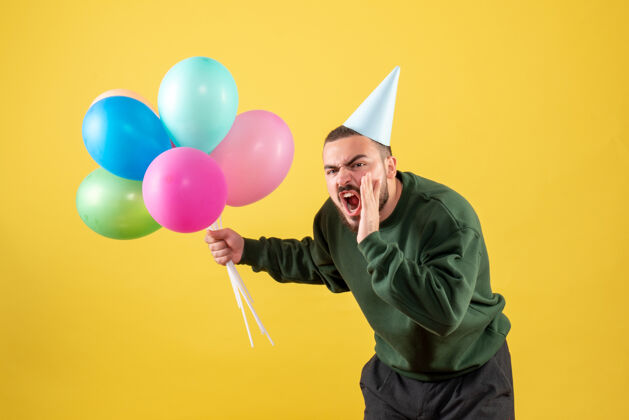 年轻男性正面图黄色背景上有彩色气球的年轻男性乐趣聚会情感
