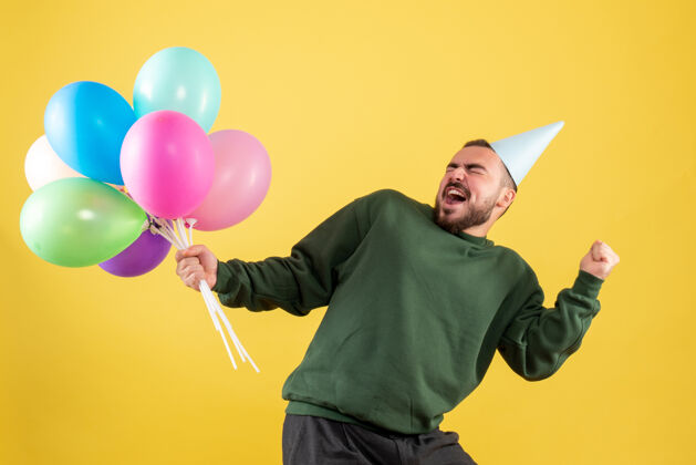 年正面图黄色背景上手持彩色气球的年轻男性庆祝聚会公园