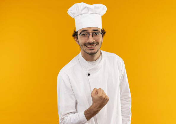 厨师面带微笑的年轻男厨师穿着厨师制服 戴着眼镜 在黄色的墙上显示“是”的手势穿着表演制服