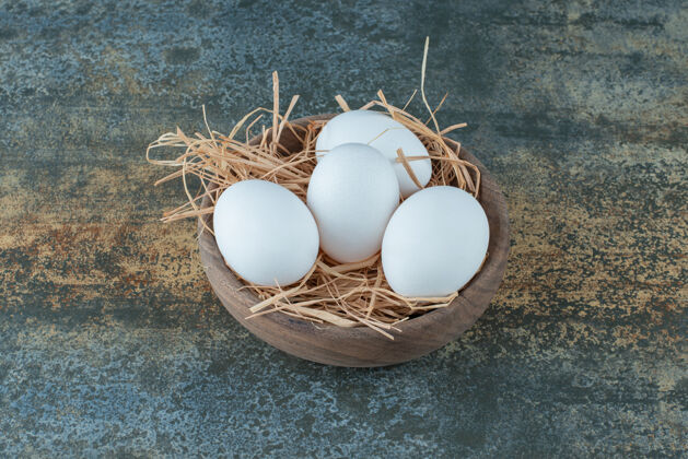 自然新鲜的鸡蛋躺在干草木碗上生的蛋白质鸡蛋