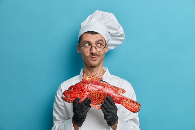 专业积极体贴的男厨师手握大鱼 想着晚餐做什么 选择健康的海鲜 美味的产品男人蓝色厨师