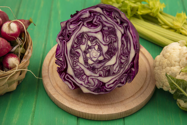 食物顶视图：新鲜的紫色卷心菜放在木制的菜板上 萝卜放在桶上 菜花和芹菜被隔离在绿色的木墙上膳食花椰菜萝卜