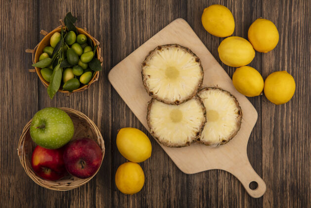 五颜六色新鲜菠萝放在木制的厨房板上 金盏花放在桶上 五颜六色的苹果放在桶上 柠檬被隔离在木墙上苹果板膳食