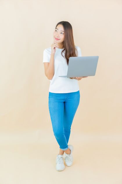 休闲肖像美丽的亚洲年轻女子用笔记本电脑在米色冲浪聪明房子