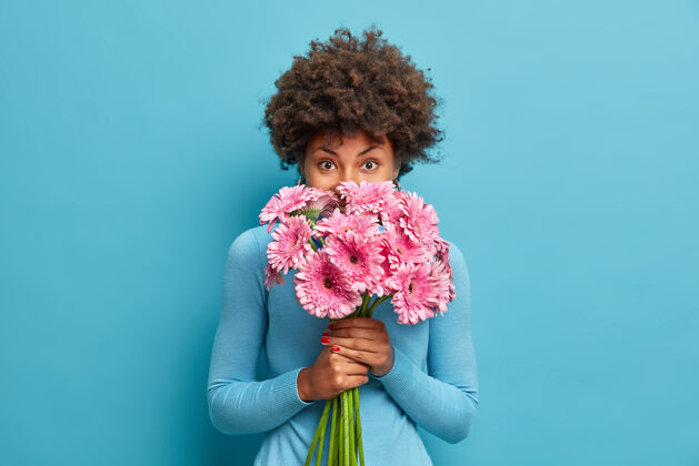 礼物美貌娇嫩的非洲裔美国女人闻着玫瑰色的非洲菊花 手拿花束享受着宜人的气味姿势花束可爱